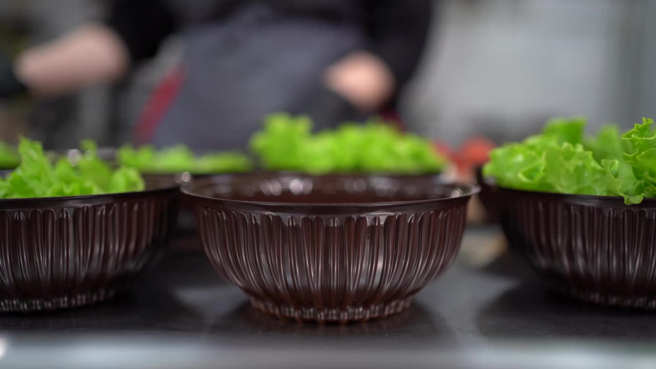 食物已经准备好了。在餐厅，厨师准备食物，并准备在一次性午餐盒。特写的手在手套放一片生菜叶子。视频素材