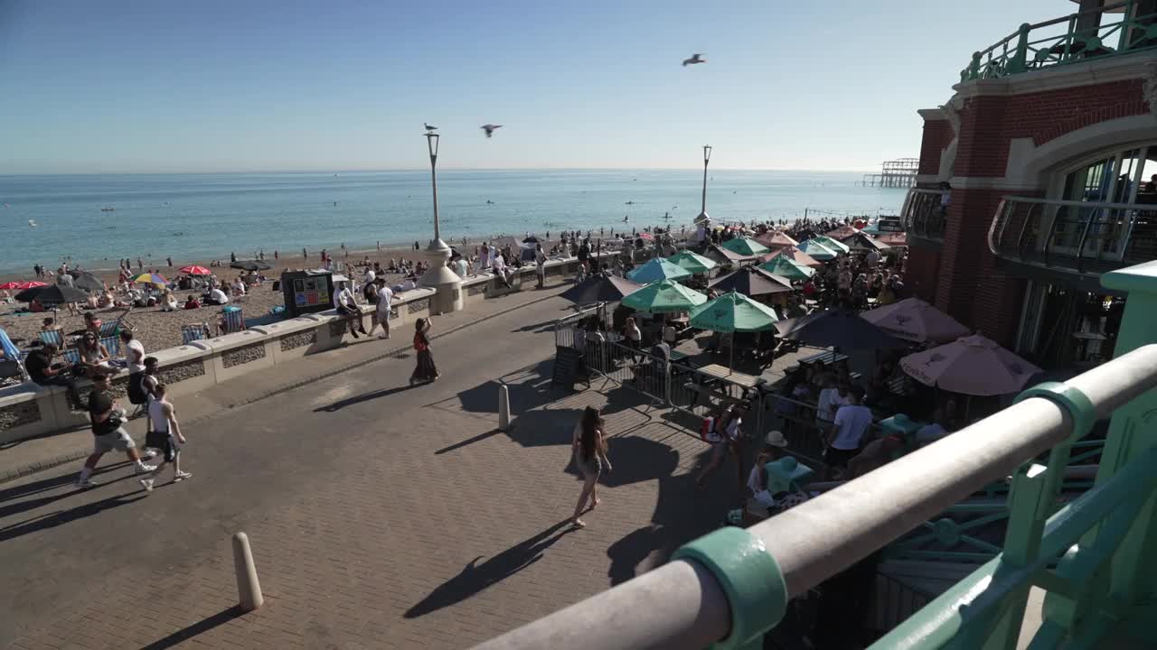 沿着步道的人和海滨景点与海滩的背景，布莱顿，苏塞克斯，英格兰，英国，欧洲视频素材