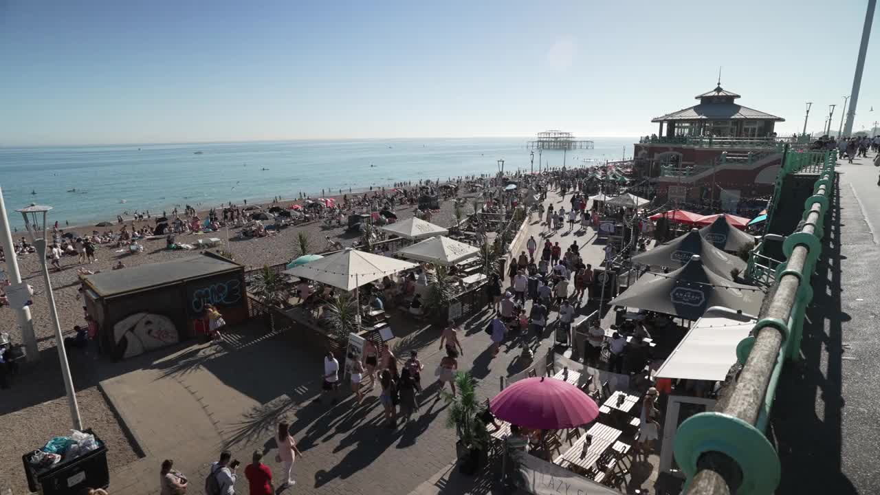 沿着步道的人和海滨景点与海滩的背景，布莱顿，苏塞克斯，英格兰，英国，欧洲视频素材