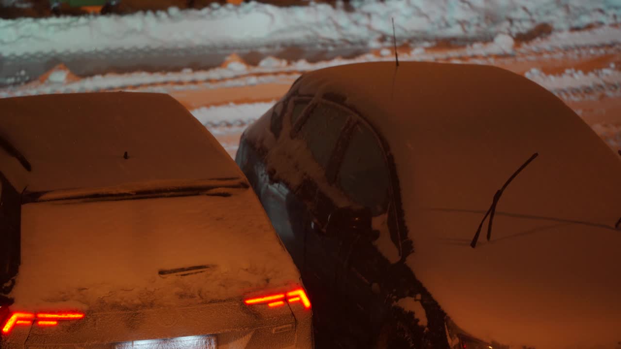 冬天，停车场的路灯下停着的汽车在黄昏时被雪覆盖。城市街道上的大雪。视频素材