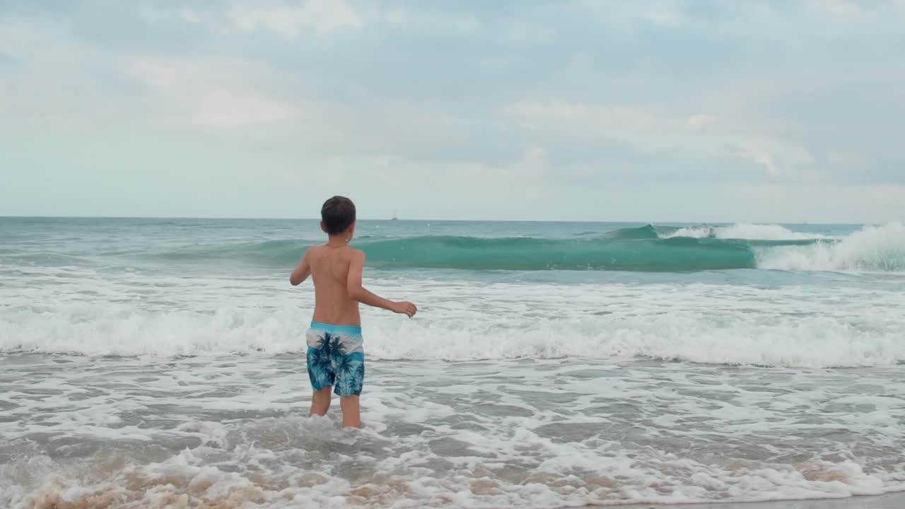 快乐的男孩在海浪中玩耍。快乐的青少年在海滩享受时光。视频素材