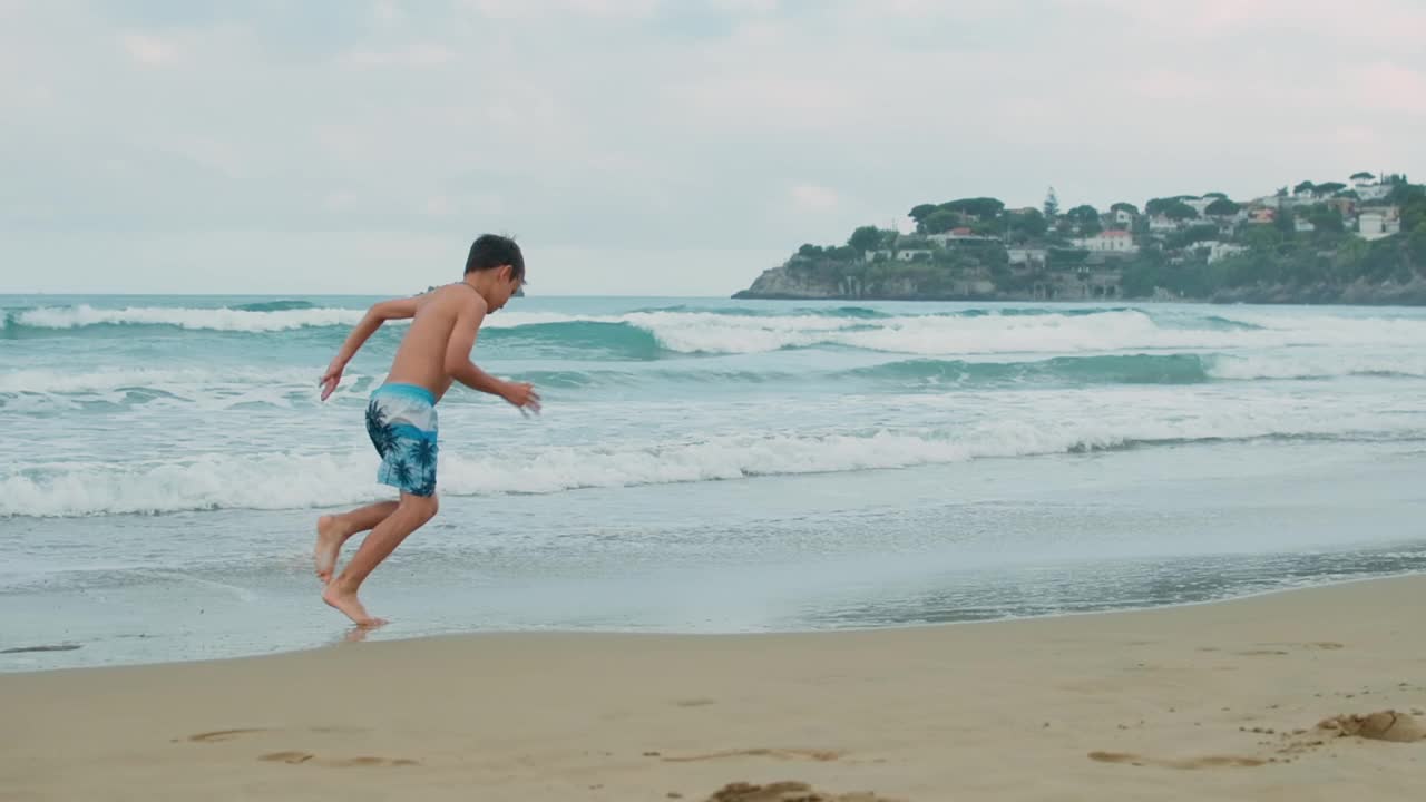 快乐的男孩在海滩享受夏天的活动。沿着海浪奔跑的家伙。视频素材