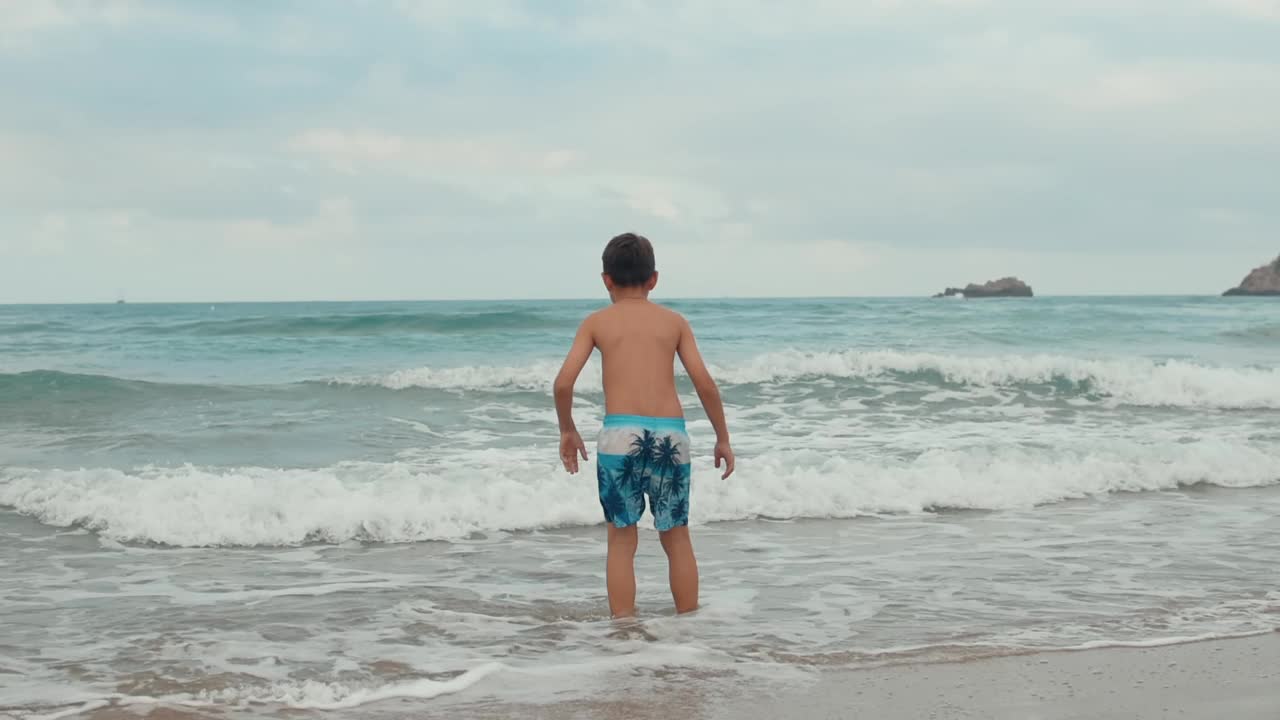 快乐的男孩在海滩享受夏天。在海边在波浪中跳跃的快乐男孩。视频素材