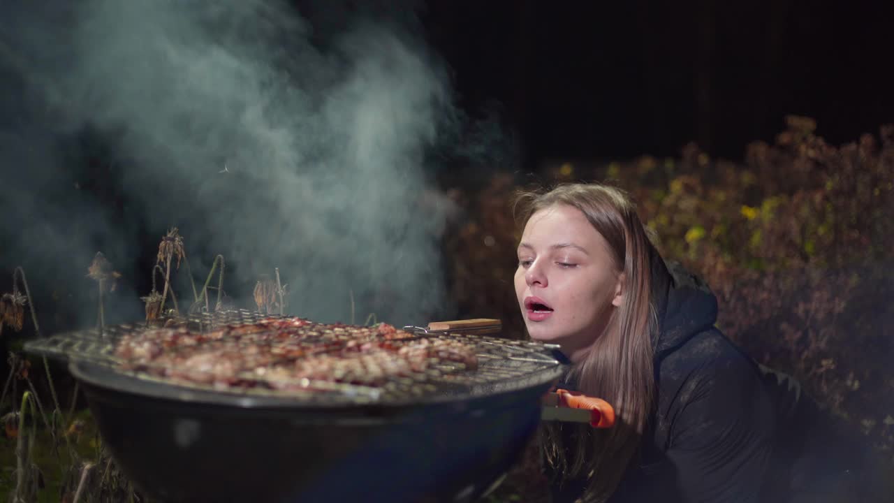 女孩一边烤烤肉，一边扇着火视频素材