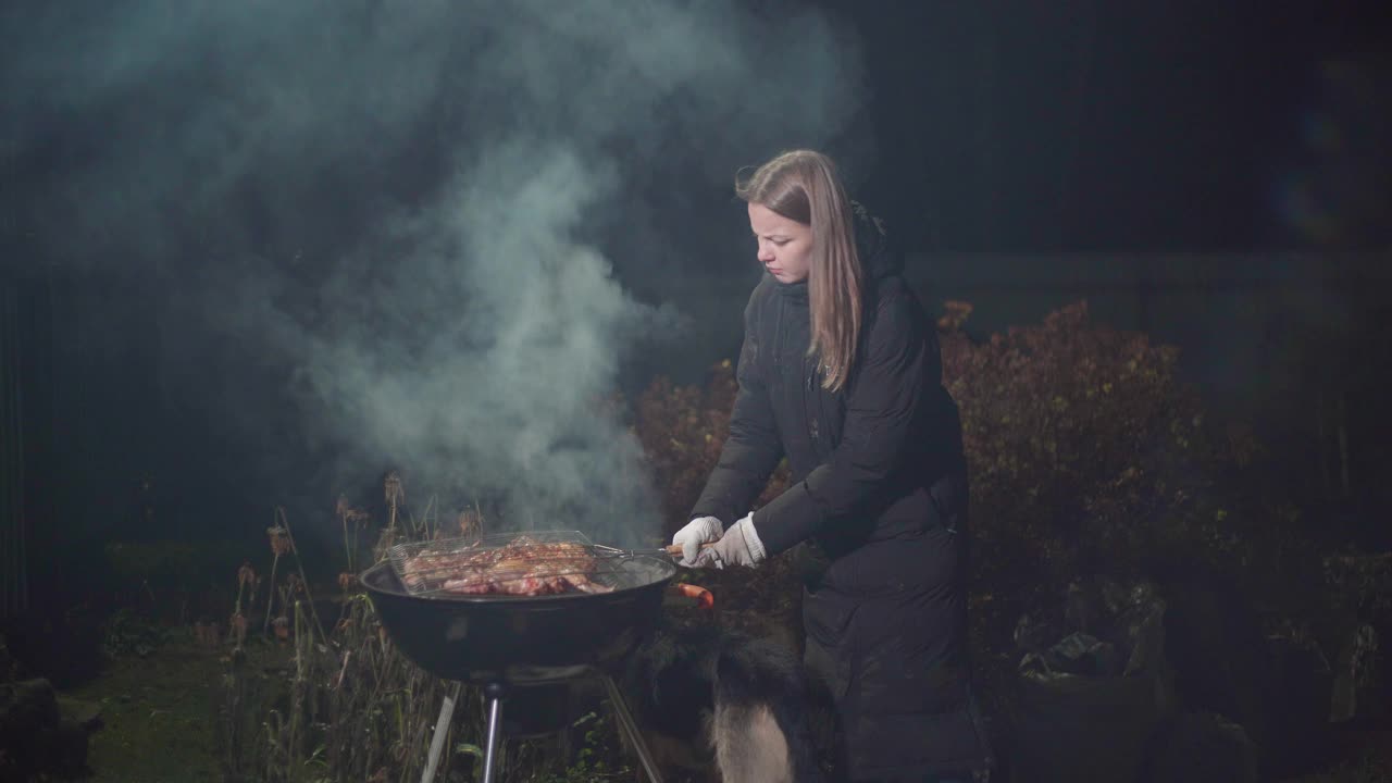 女孩一边烤烤肉，一边扇着火视频素材