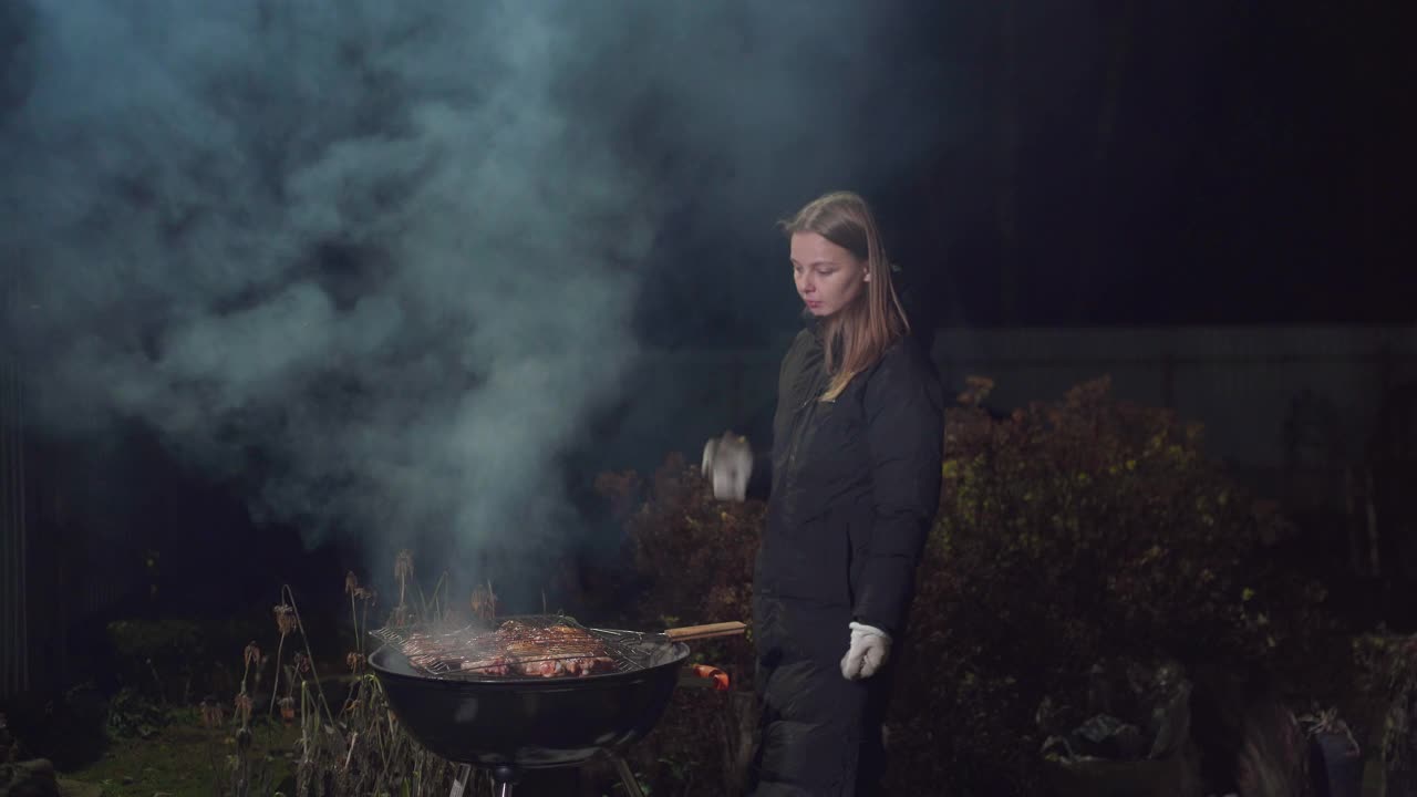 女孩一边烤烤肉，一边扇着火视频素材