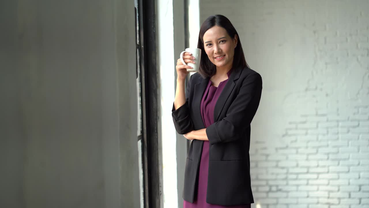 亚洲女商人喝咖啡站在窗口附近的咖啡馆看着相机视频素材