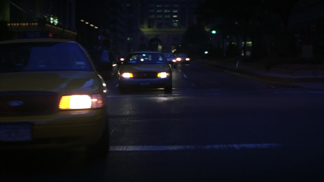 加工车牌后的汽车，出租车行驶在纽约市的街道和十字路口。头灯。高层建筑与灯光在bg可见。视频素材