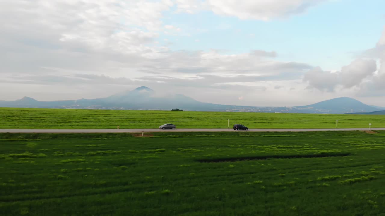 无人机航拍画面:黑色汽车行驶在农田和绿色乡村之间的道路上，无人机紧随其后。视频素材