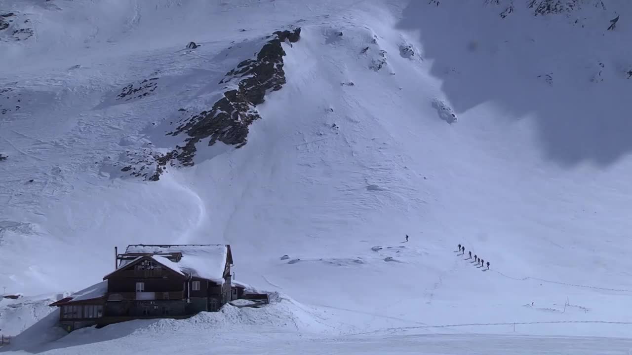 一群徒步旅行者从他们离开的地方出发，走在白雪覆盖的斜坡上视频素材