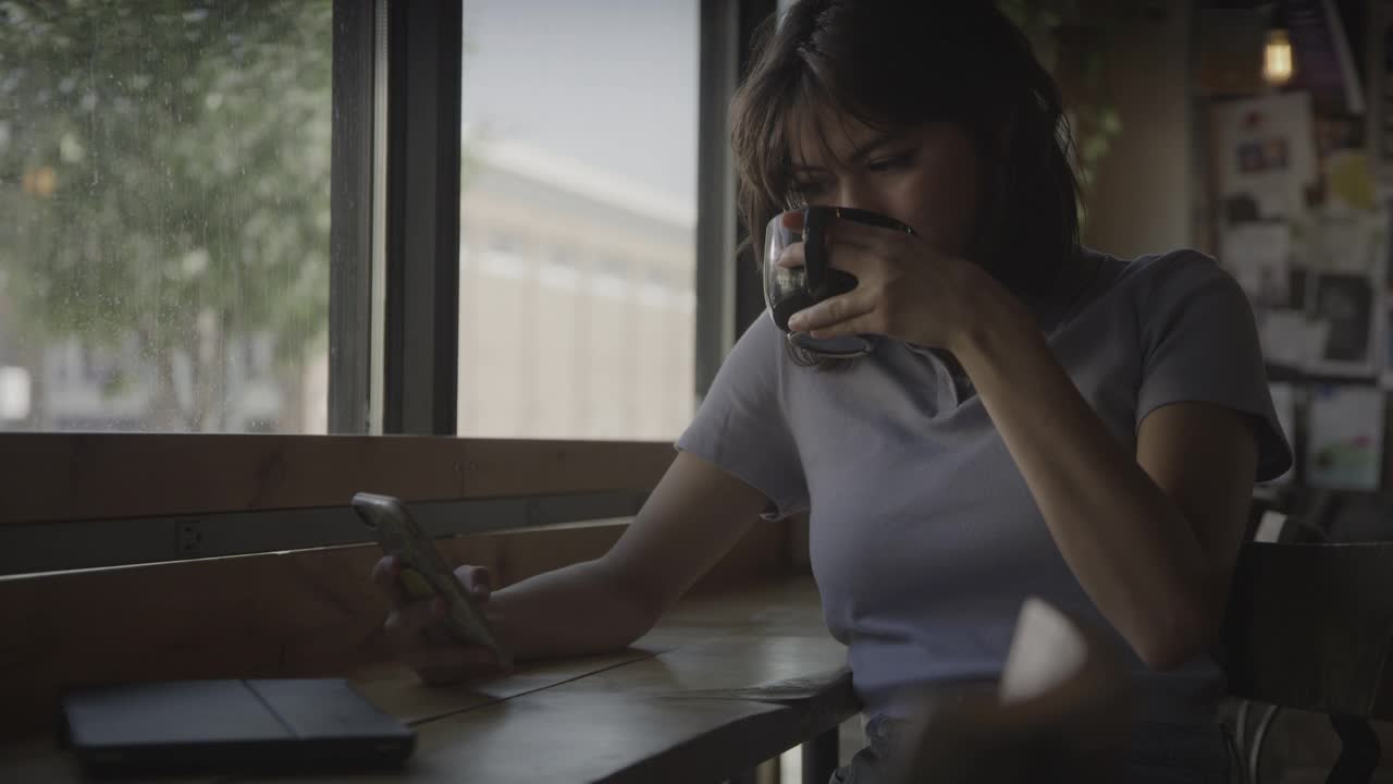 美国犹他州普罗沃，一名女子在咖啡馆里喝酒，对着手机大笑视频素材