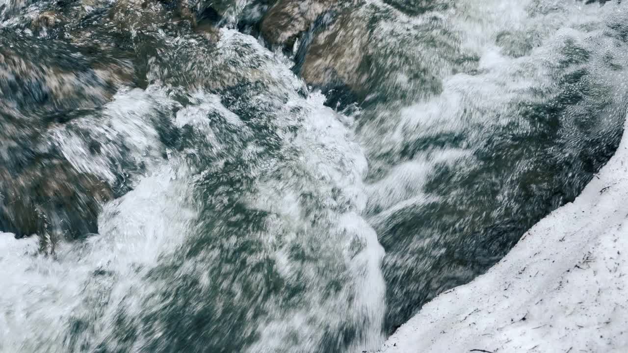 在冬天的雪中潺潺的河水。特写湍急、结冰的河流和积雪的河岸。视频素材