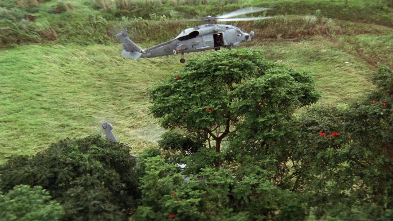 sh-60b美军海鹰直升机在草地上空盘旋。第二架直升机在地面。热带。树。视频素材