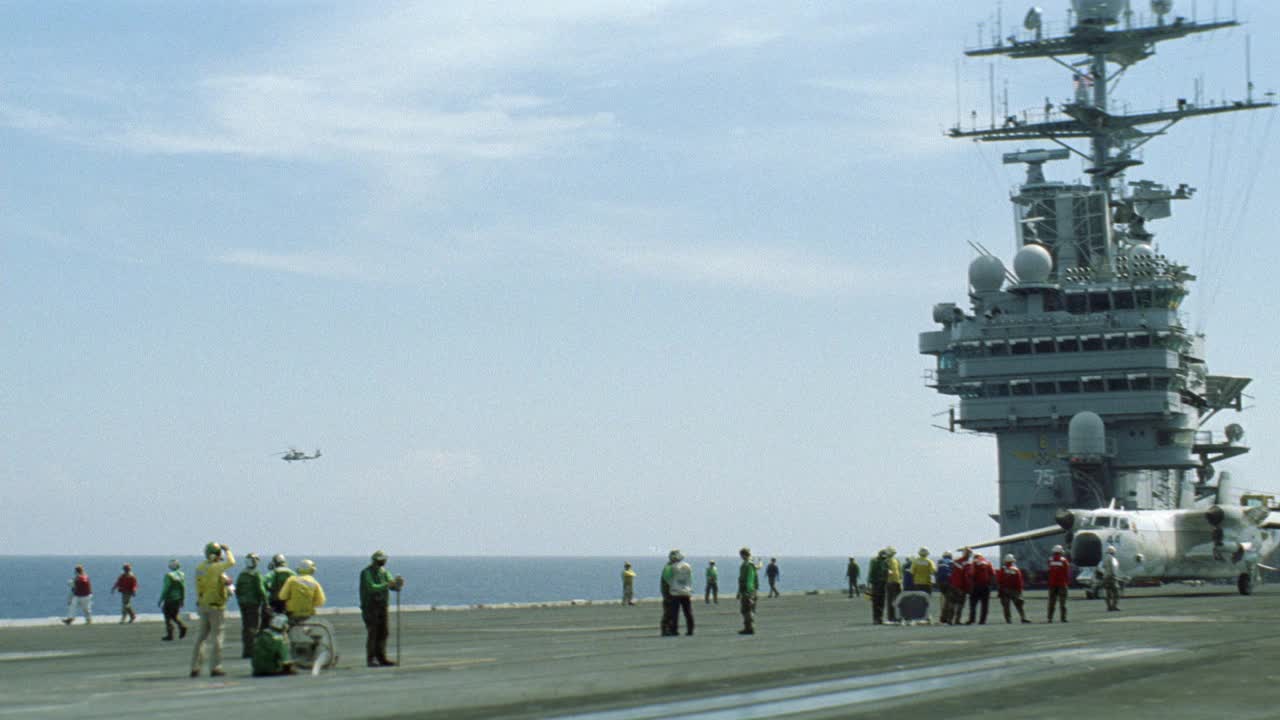 c-2a灰狗飞机从哈利s.杜鲁门号航空母舰的飞行甲板上滑行的广角镜头。机组人员协助。雷达塔和卫星在bg。大海，蓝天，白云。Sh-60b海鹰直升机在船侧飞过。航空母舰。视频素材