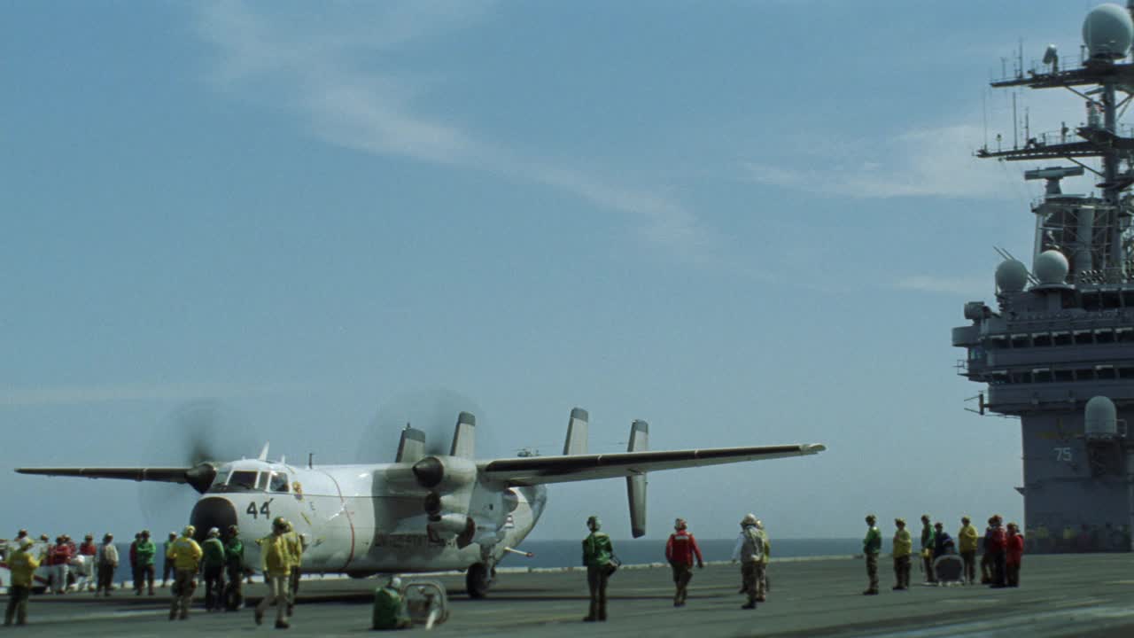 c-2a灰狗飞机从哈利s.杜鲁门号航空母舰的飞行甲板上滑行的广角镜头。雷达塔和卫星在bg。大海，蓝天，白云。Sh-60b海鹰直升机在船侧飞过。航空母舰。视频素材