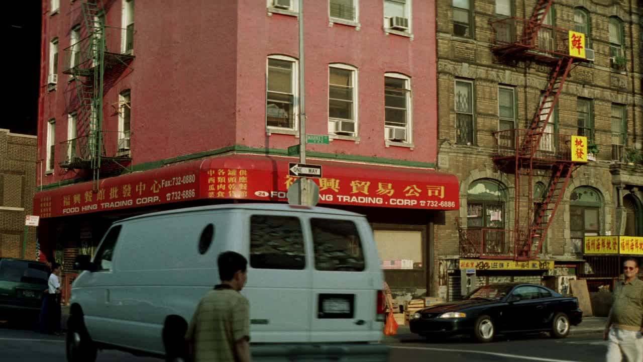 广角的汽车行驶在城市街道和人们走在人行道前的多层砖建筑在低阶级地区。在建筑物的侧面可以看到用中文写的防火梯和标志。会是一层有商店的公寓楼吗视频素材