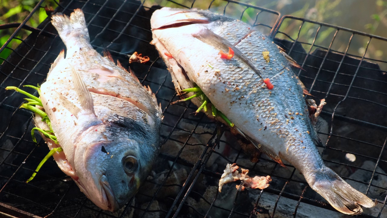 用香喷喷的香料在烧烤架上烹煮海鲜。库克将海鲈鱼切碎后撒上少量的香料视频素材