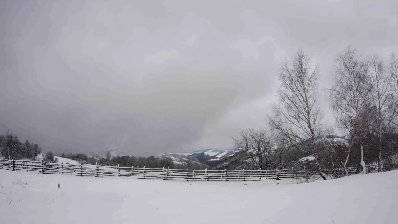 冬天的风景是森林和白雪覆盖的栅栏，铅灰色的云爬上山谷并穿过它们视频素材