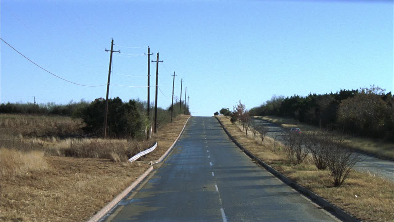 广角的乡村道路在农村地区，作为旧型号的雪佛兰或雪佛兰卡车行驶在道路上。路边的草枯萎了。电线杆。可能是乡村公路。马路另一边的车。视频素材