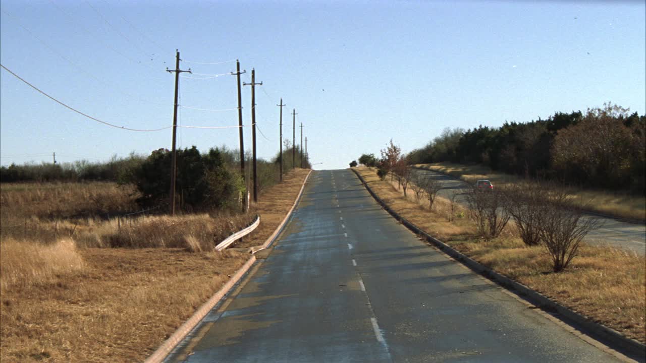 广角的乡村道路在农村地区，作为旧型号的雪佛兰或雪佛兰卡车行驶在道路上。路边的草枯萎了。电线杆。可能是乡村公路。马路另一边的车。视频素材