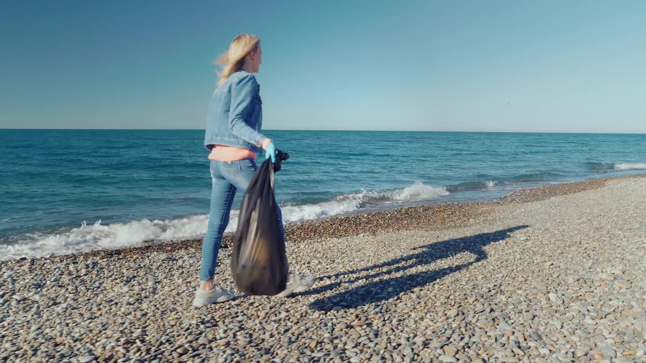 一位女性志愿者用黑色垃圾袋收集垃圾。视频素材