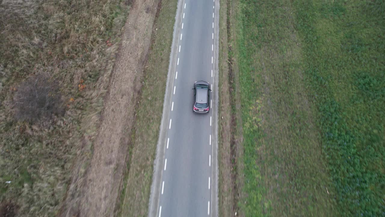 汽车正行驶在穿过田野的道路上，无人机拍下了鸟瞰图。秋天的时候在柏油路上，镜头跟着车走。视频素材