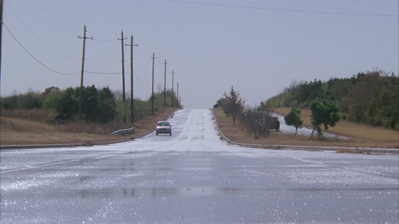 宽阔的乡村角一条潮湿的乡间小路，仿佛最近下过雨。小汽车、小货车、旅游巴士或校车都会经过。夹头与潮湿路面的闭合角度。多云的天空。电线杆、树木。视频素材