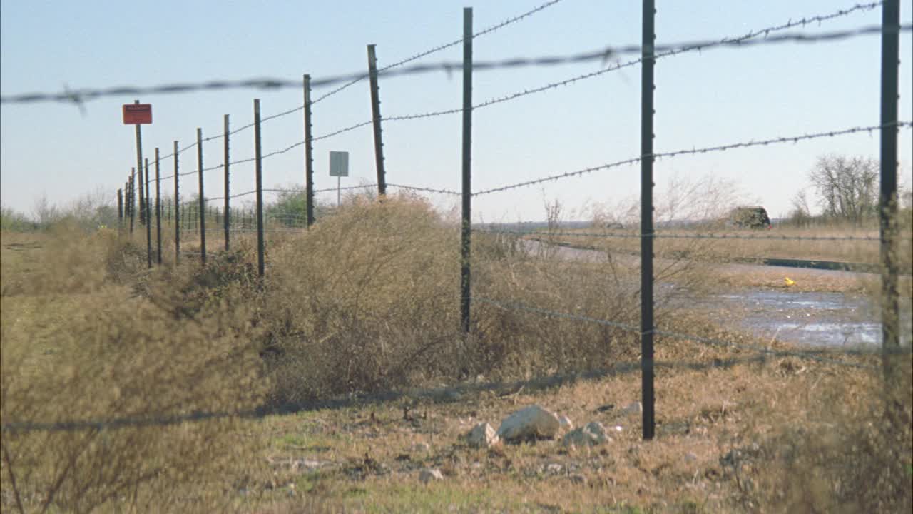 广角的汽车沿着乡村公路或划分高速公路在一个大风天描绘吹刷。Ê校车部分可见。碧蓝的天空，近角的铁丝网。视频素材