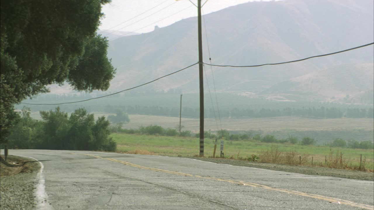 广角的汽车，suv迷你货车或小卡车沿乡村道路在农村地区。山的背景。可见树木、灌木丛、田野、电线杆、带刺铁丝网。德州的路牌上写着“2424号农场路”，表示有农田。标志视频素材