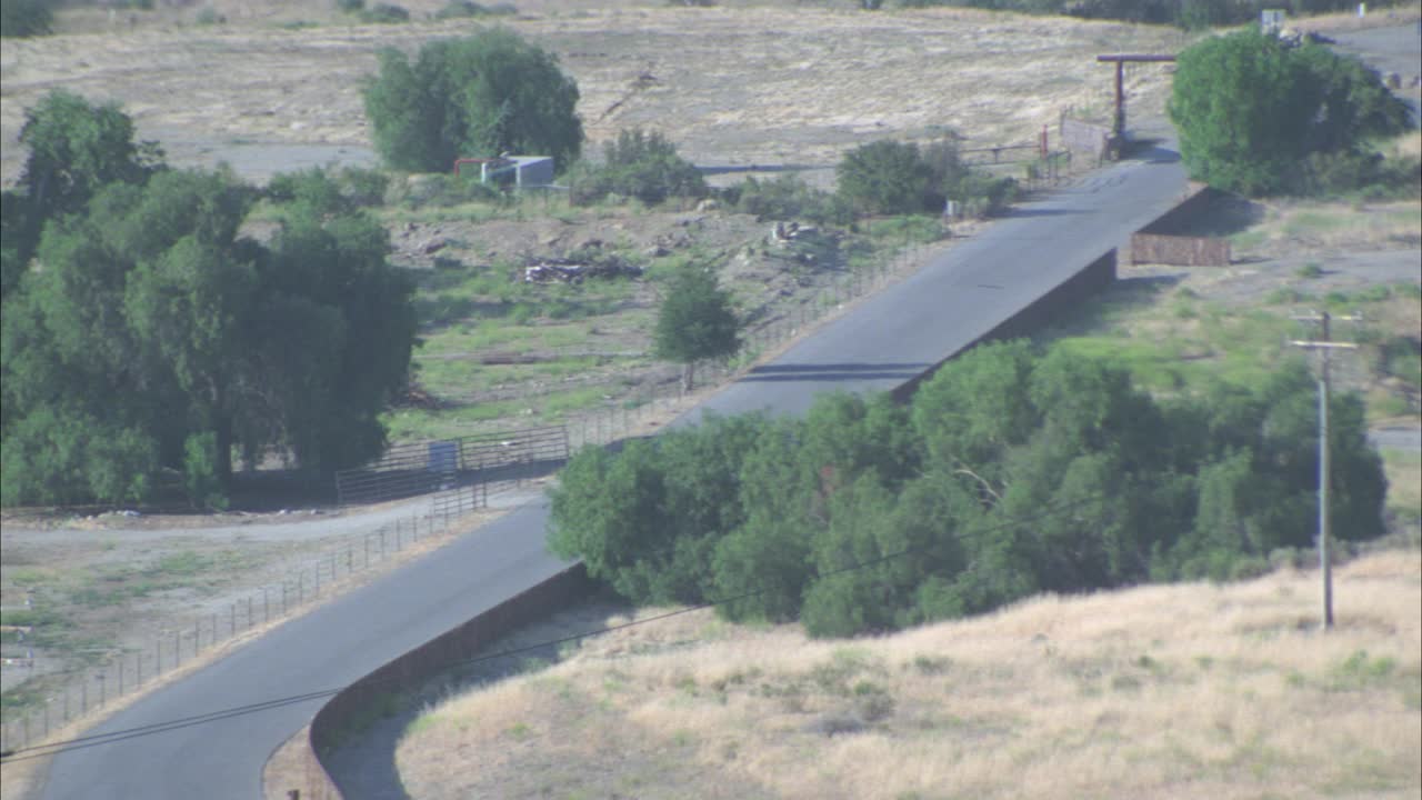 在农村地区，一辆小汽车、小型越野车或小型卡车沿着乡村道路行驶的航拍图。可见树木、田野、灌木丛、旧油罐。视频素材