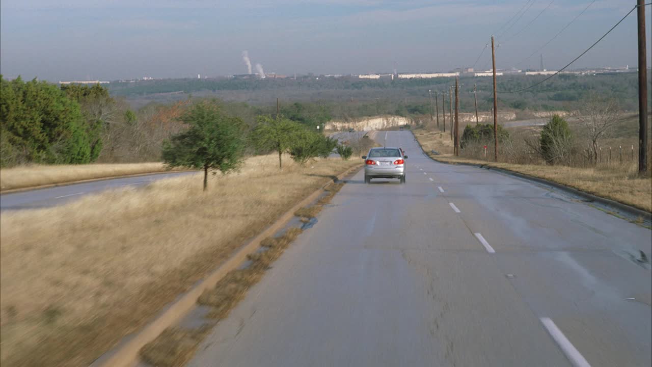 广角移动的汽车和卡车行驶在农村或乡村道路。可能是追逐，也可能是追逐。在bg中可见的城市或工业区。可能是工厂。视频素材