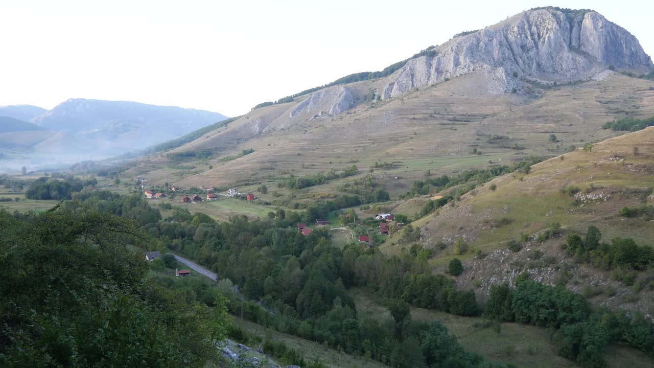 山景:山脚下有多岩石的山峰，一条道路蜿蜒穿过绿色的森林，在森林的边缘建造了度假屋和小木屋视频素材