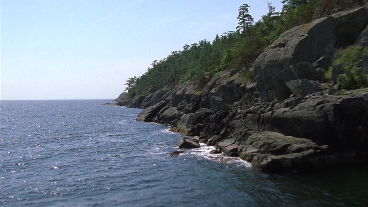 由海湾或湖泊环绕的岛屿海岸线的空中分布。多岩石的海岸线。可见树木或森林。视频素材