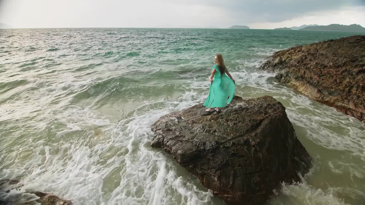 女人走在礁石上的海礁石，暴风雨多云的海洋。蓝色泳衣连衣裙束腰外衣。概念休息，热带度假海岸线旅游夏季假期视频素材