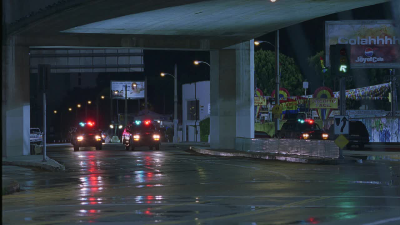 从右到左，三辆警用越野车闪烁着警灯或警笛在城市街道上行驶。越野车从桥下或立交桥下行驶，在潮湿的街道上转弯。可能是因为下雨。越野车相撞。汽车特技表演。视频素材