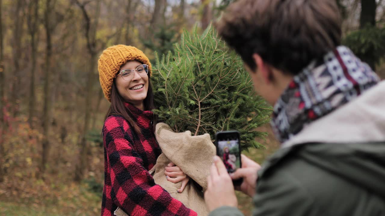 男友在树林里给女友和他们新买的圣诞树拍照视频素材