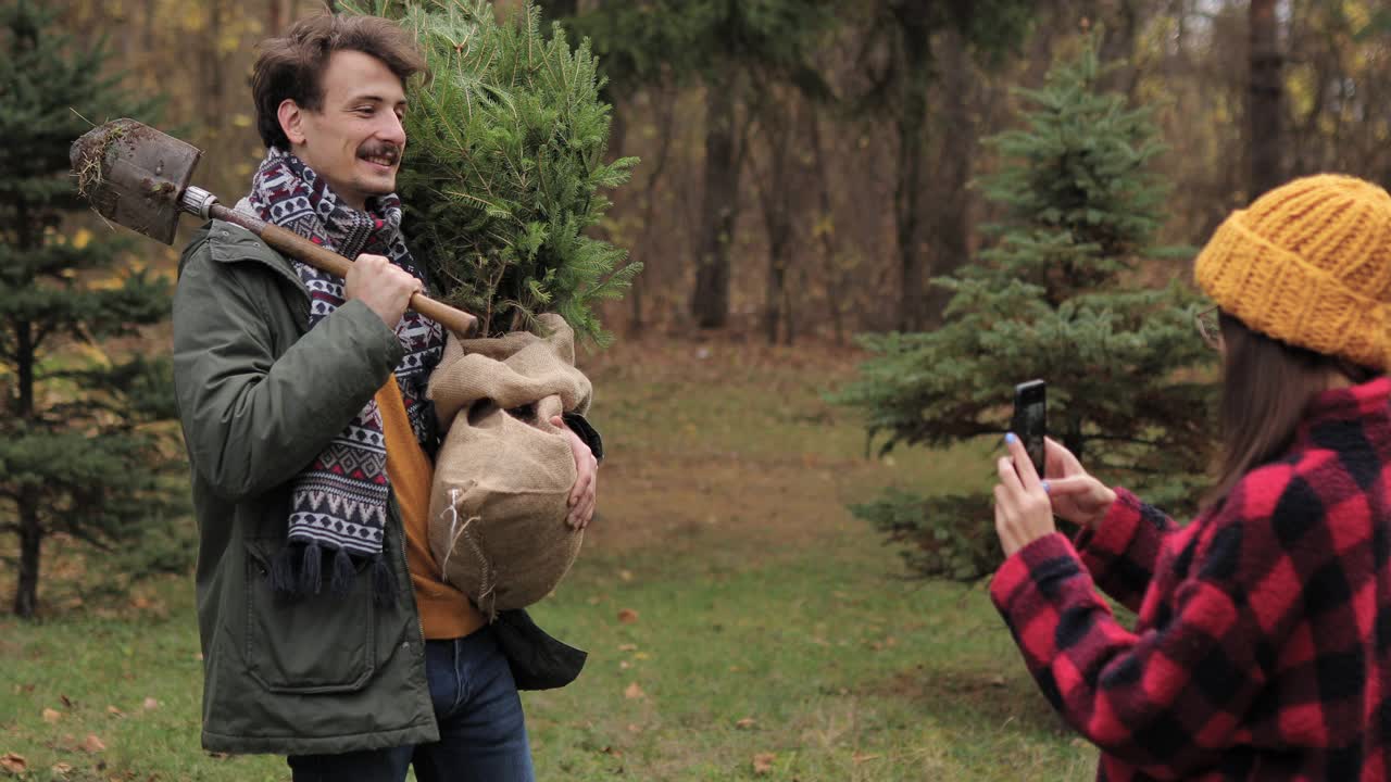 女友在树林里给男友和他们新买的圣诞树拍照视频素材