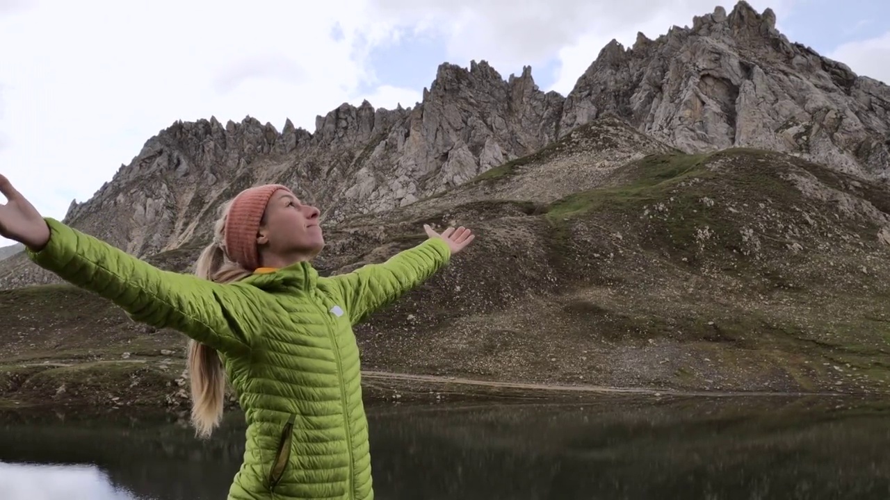 一个年轻的受鼓舞的女人站在山顶的湖面上举起双手。女性徒步旅行者享受简单的生活视频素材