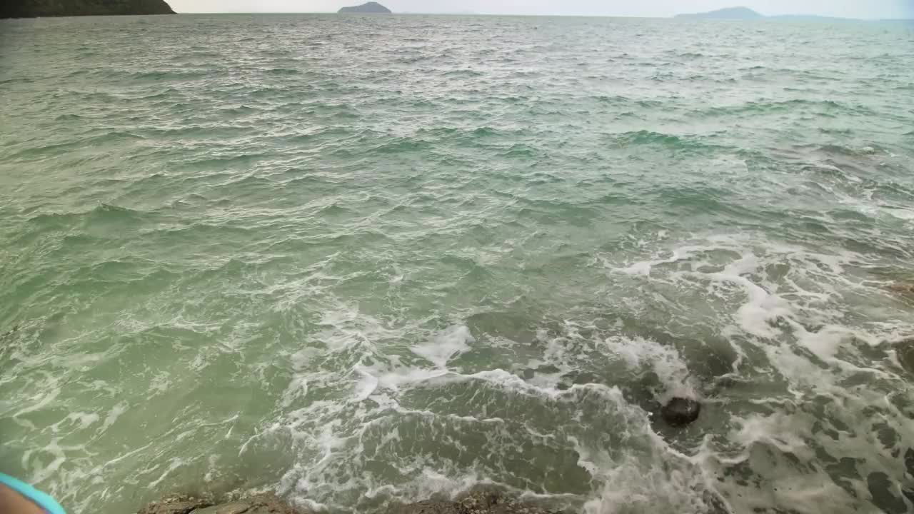 女人冷放松休息在礁石上的海礁石，暴风雨多云的海洋。女人在泳装连衣裙束腰外衣。概念休息热带户外旅游视频素材