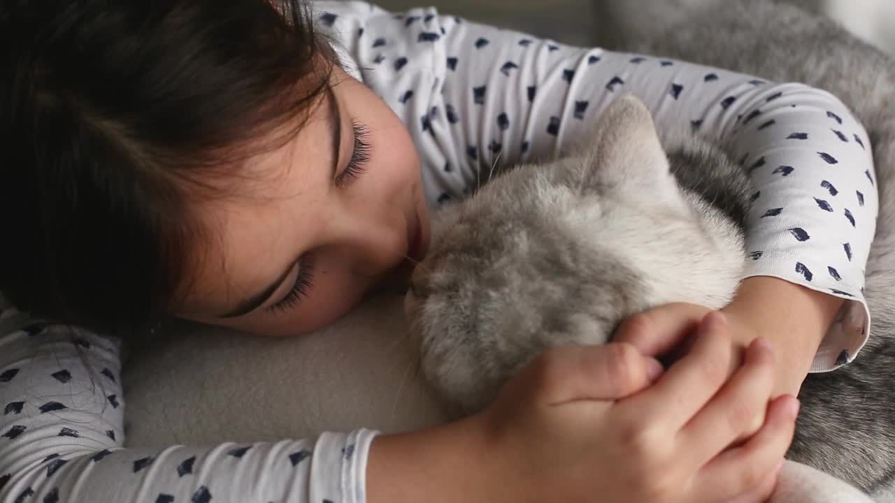 在清晨的阳光下，黑发的小女孩躺在床上，抱着床上的一只白猫视频素材