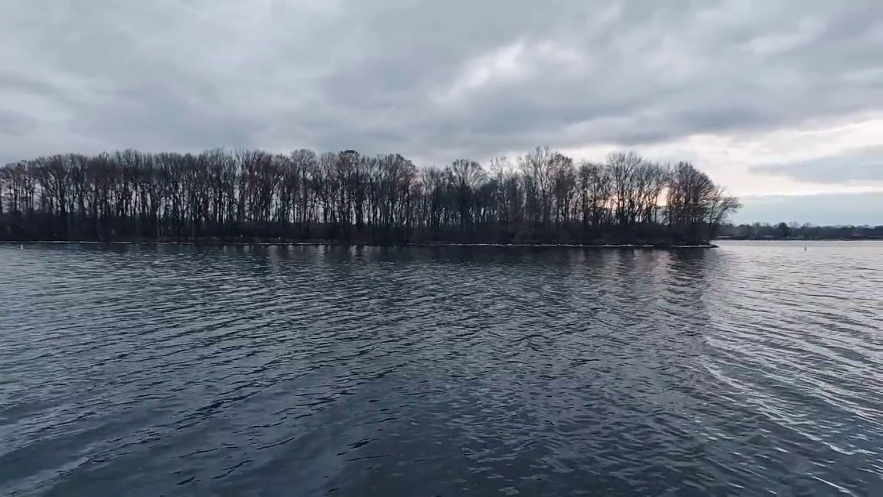 岛上冬天光秃秃的树木的剪影。遥望海军蓝的冬季湖水在地平线上汇合。阴暗的,喜怒无常的天空。视频素材