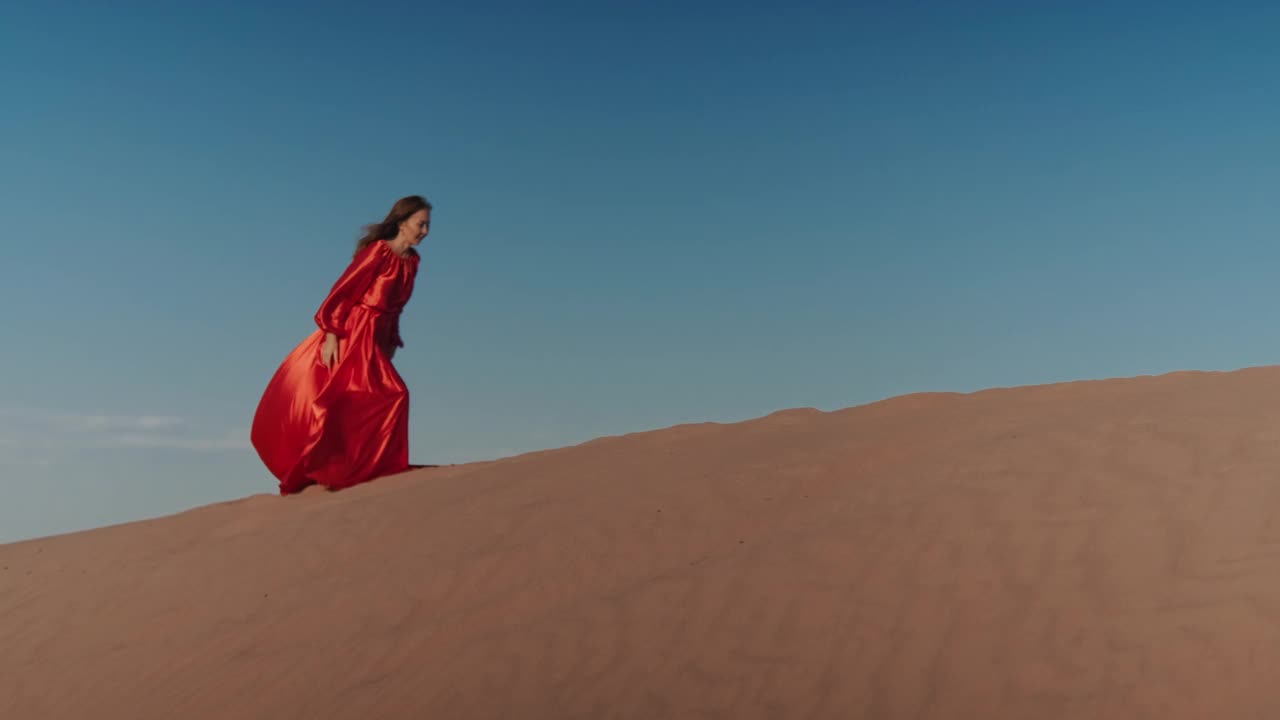 一个穿着红色裙子的亚洲女人在沙丘上跳舞视频素材