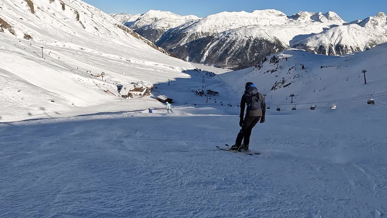 慢镜头:跟随镜头，一个年轻人在阿尔卑斯山的滑雪坡上滑雪下坡。视频素材