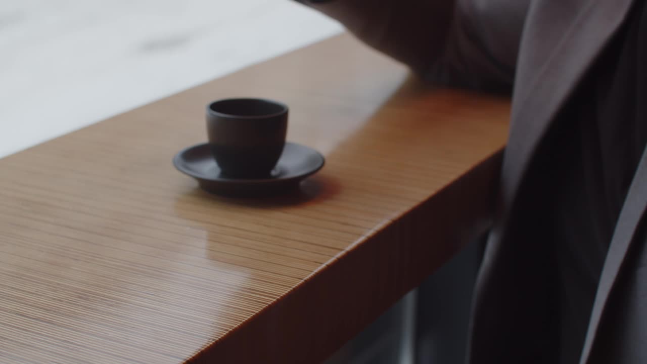 一个男人坐在咖啡馆里，拿着一杯咖啡看着他的手表视频素材