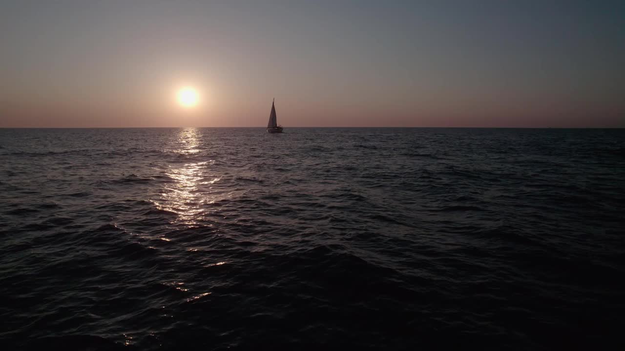 日出在海面上，相机在水面上飞行。一艘帆船缓缓地顶着天空航行。视频素材