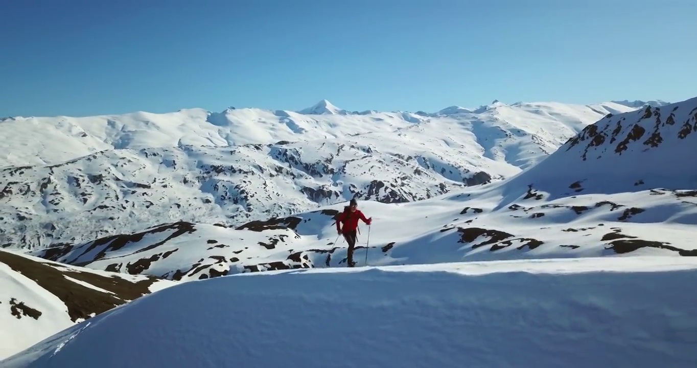 空中摄影:男性游客在山上拄着滑雪杖行走，无人机在白雪之上飞行视频素材