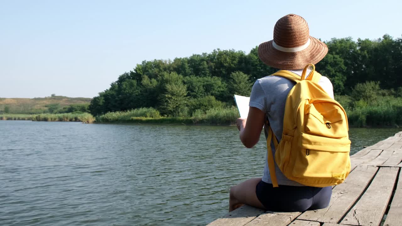 背包旅行者，手拿地图，坐在森林中横跨河流的木桥上休息。夏天的旅行。享受自然风光的女游客视频素材