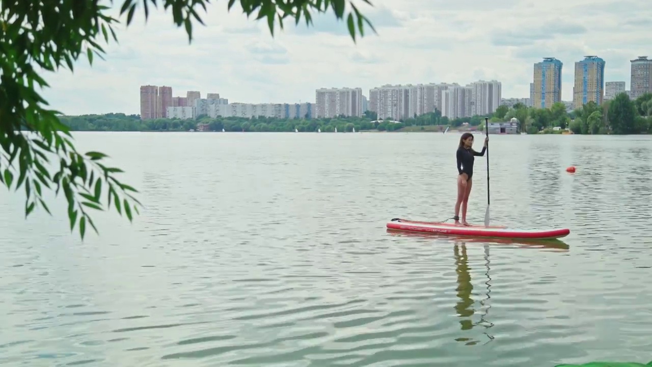 穿着黑色泳装的女人在冲浪板上。积极生活方式的概念，极限运动视频素材