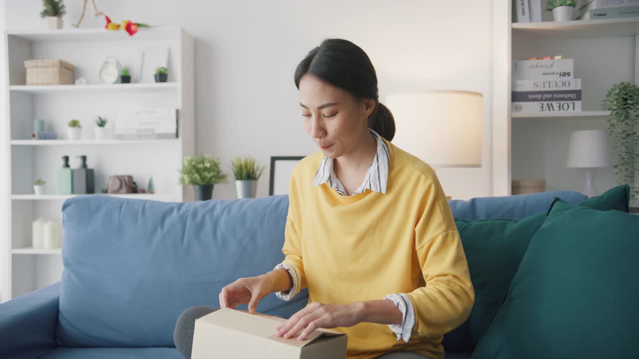 年轻女子在家中客厅沙发上打开纸箱收包裹。视频素材