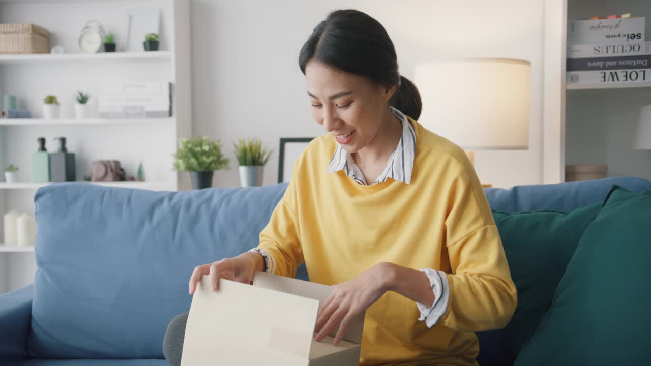 年轻女子在家中客厅沙发上打开纸箱收包裹。视频素材